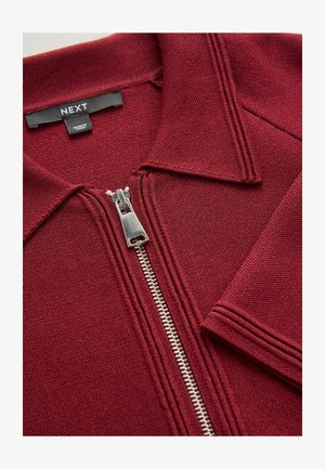 Burgundy zip-up jacket with a polo collar, textured fabric, silver zipper, and contrasting stitching near the collar and sleeves.