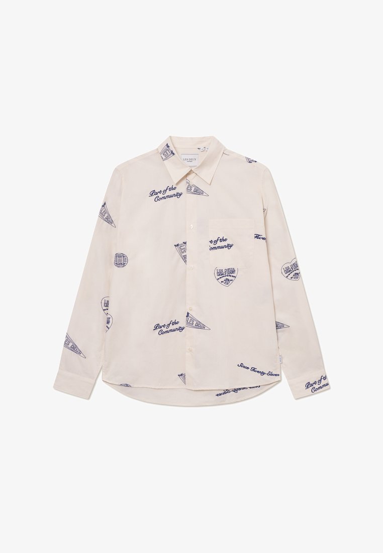 Camicia a maniche lunghe beige chiaro con grafiche e testo blu navy. Presenta colletto con bottoni e taschino sul petto. Tessuto in cotone.