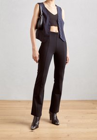 Marinblå randig väst över en svart kort topp, ihop med svarta åtsittande byxor och svarta klackboots med silverfärgade tådetaljer.