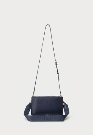 Jūras zilas ādas crossbody soma ar strukturētu siksnu, zelta furnitūru un rāvējslēdzēju. Siksnā ir smalks logotipa detalizējums.