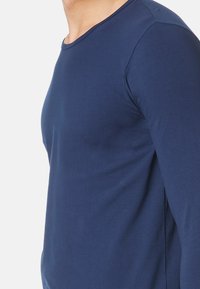 Granatowa koszula z długim rękawem, uszyta z gładkiego, lekkiego materiału. Posiada okrągły dekolt i boczne rozcięcia, które zapewniają swobodę ruchów.