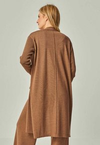 Brauner gestrickter Cardigan mit einer langen, lässigen Passform, der einen einfachen Kragen und eine Mittelnaht auf dem Rücken aufweist. Weicher Stoff und leichtes Design.