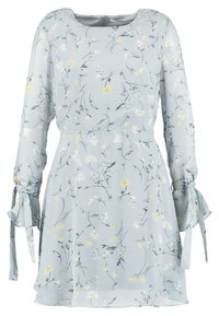 Robe florale bleu clair à manches longues, avec des poignets noués et une taille cintrée. Présente des motifs délicats de fleurs jaunes et blanches.