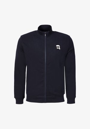 Marineblaue Jacke mit Reißverschluss, Rippbündchen an Ärmeln und Saum, mit einem kleinen weißen und schwarzen grafischen Logo auf der linken Brust.