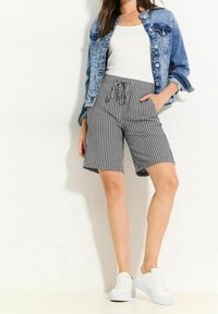 Pruhované kraťasy s tahem v pase, bočními kapsami a volným střihem, v kombinaci s denimovou bundou a bílými teniskami.