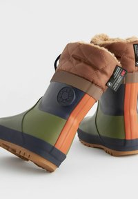 Bottes imperméables colorées avec une tige matelassée marron, un corps vert et marine, une semelle en caoutchouc et des accents texturés pour une meilleure adhérence.