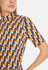 Figurbetontes Kurzarmoberteil mit einem geometrischen Muster in Orange, Blau, Braun und Creme, mit hohem Kragen und glatter Stofftextur.