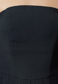 Robe noire sans bretelles avec une texture lisse et un corsage ajusté. Présente une jupe plissée à l'ourlet. Conçue pour une silhouette élégante.