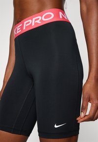 Fekete kompressziós rövidnadrág, rózsaszín elasztikus derékkal, amelyen a "NIKE PRO" felirat található, és fehér Nike logó a szegélyen.
