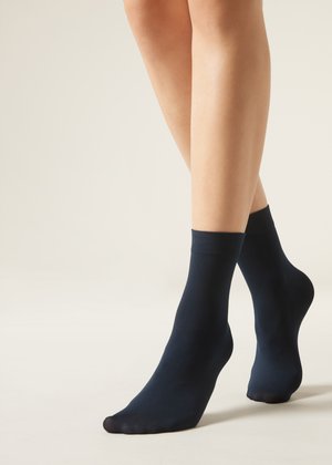 Gambe con calzini neri alla caviglia, in piedi su uno sfondo chiaro e semplice.