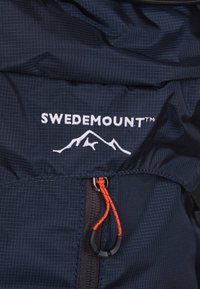 Sac à dos en tissu bleu marine arborant le logo "SWEDEMOUNT" en blanc, avec une tirette de fermeture éclair orange vif et un motif texturé.