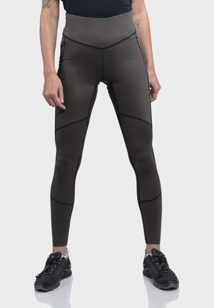 Hochtaillierte schwarze Leggings mit einer glatten, matten Textur. Verfügt über schräg verlaufende Nähte und kontrastierende Linien. Kombiniert mit schwarzen Sportschuhen.