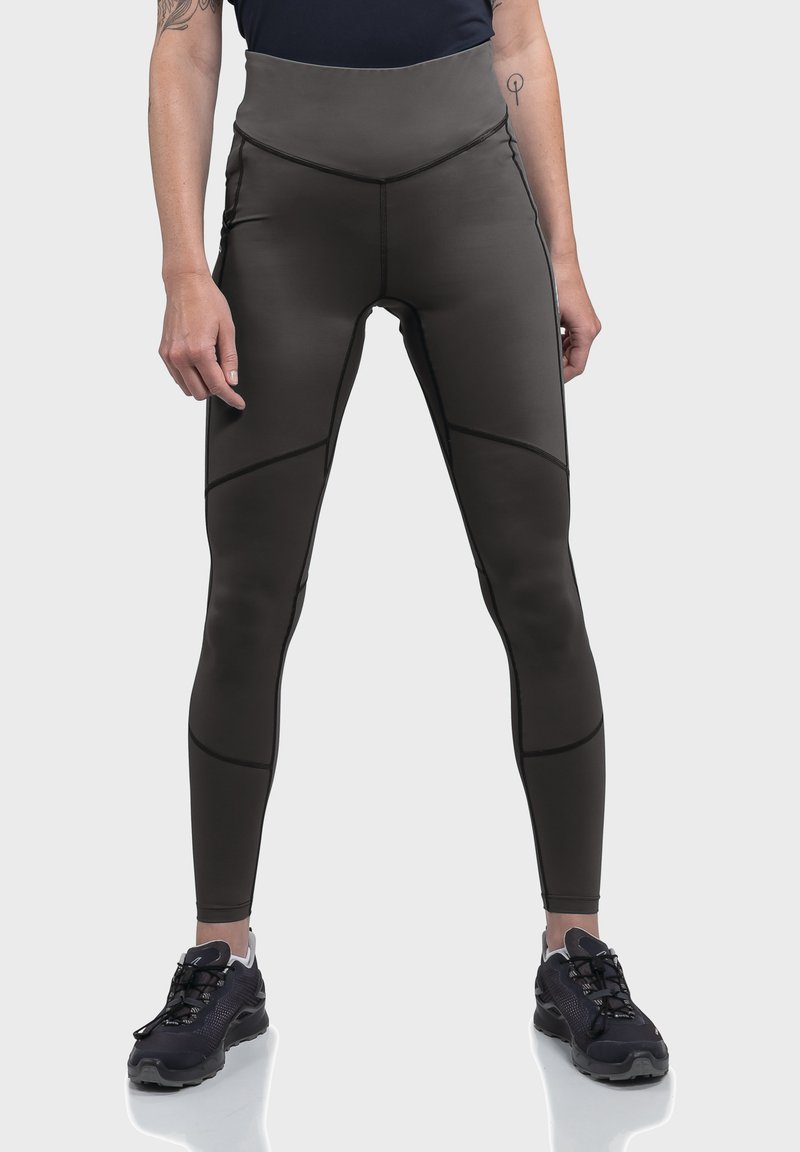 Hochtaillierte schwarze Leggings mit einer glatten, matten Textur. Verfügt über schräg verlaufende Nähte und kontrastierende Linien. Kombiniert mit schwarzen Sportschuhen.