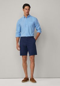 Light blue button-up shirt with rolled sleeves, navy shorts, and brown loafers. Simple design, smooth texture, and no visible patterns.