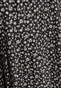 Musta kangas, jossa pieni valkoinen kukkakuvio. Hieman teksturoitu ja laskostettu design, joka lisää ulottuvuutta ja liikkeen tuntua.