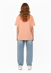T-shirt oversize pesca con maniche corte, abbinata a jeans a gamba larga blu chiaro. Sneakers bianche completano l'outfit. Silhouette semplice e rilassata.