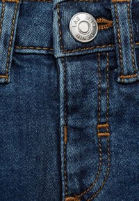 Jeans din denim albastru închis cu cusături portocalii contrastante, având un sistem de închidere cu un buton argintie și un talie cusută.