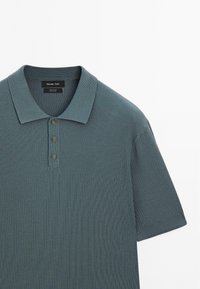 Koszulka polo z prążkowanej, ciemnoturkusowej bawełny, z kołnierzykiem i plisą na trzy guziki. Krótkie rękawy z bezszwowymi krawędziami.