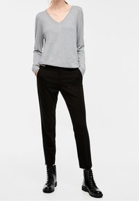 Grijze V-halstrui met lange mouwen, gecombineerd met zwarte taps toelopende broek en zwarte veterschoenen. De materialen lijken glad en casual.
