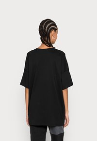 T-shirt nera oversize in cotone, con scollo rotondo, maniche corte e un design semplice senza motivi o dettagli visibili.