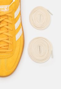 Kollane nahkking, millel on valged triibud, tekstureeritud materjal ja ümmargused beežid najad kinga kõrval.