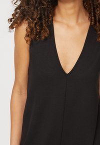 Top negro sin mangas con un diseño de escote en V profundo, hecho de una tela suave. Presenta una costura central y un ajuste relajado.