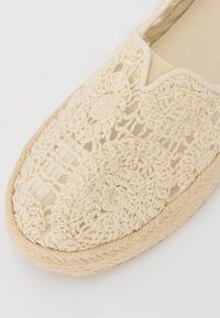 Beigiškai nertos espadrilės su apvalia forma, tekstūruotu viršumi ir pintu jūros dumblio padu. Lengvas audinys su išsamiu gėlių raštu.