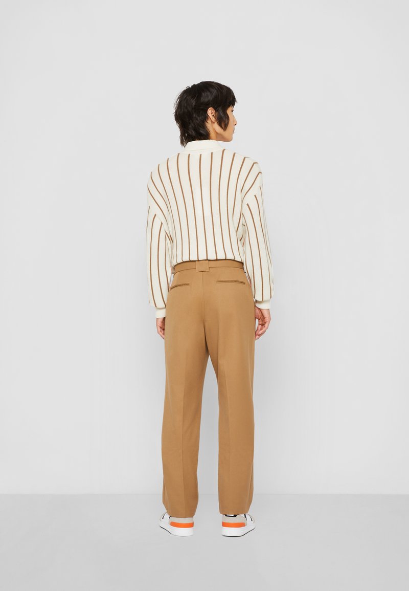 Sweater de mezcla de lana con rayas beige verticales, combinado con pantalones marrones de talle alto y pernera ajustada, y zapatillas blancas con un acento naranja.