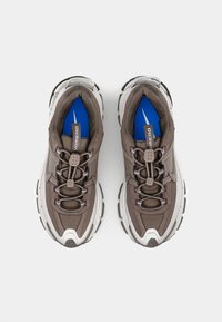 Καφέ αθλητικά παπούτσια με κορδόνια, με υφή στο επάνω μέρος, λευκές λεπτομέρειες και μπλε σόλα με λογότυπο σε γκρι χρώμα. Σχεδίαση χοντρής σόλας.