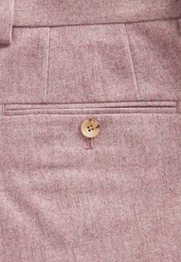 Rosa Wollhose aus strukturiertem Stoff mit Fronttaschen und einem einzelnen runden Knopfverschluss mit vier Löchern. Sichtbare, saubere Nähte.