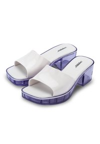 Chanclas de plástico blancas con una correa ancha, tacones de bloque transparentes en color púrpura y una suela texturizada geométrica. Logotipo en la plantilla.