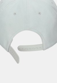 Gorra gris claro con una tela texturizada, que cuenta con una correa ajustable de plástico con múltiples agujeros para el tamaño y pequeñas ojales de ventilación.
