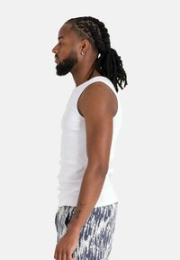 Top senza maniche bianco realizzato in tessuto a coste, abbinato a pantaloni corti stampati con una combinazione di colori blu e bianco, mostrato in vista profilo.