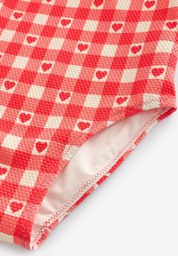 Rotes und cremefarben kariertes Stoffmuster mit strukturierter Oberfläche und kleinen Herzen, versehen mit einem glatten Innenfutter und kontrastierendem Zierstich.