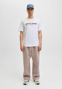 Tricou alb din bumbac cu logo-ul "JACK&JONES", pantaloni largi bej și o șapcă de culoare bleu deschis. Încălțămintea are un design robust cu accente bej.