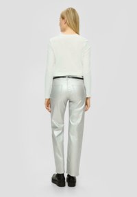 Zilverkleurige rechte broek met een gladde textuur, gecombineerd met een witte blouse met lange mouwen en een zwarte riem, gezien vanaf de achterkant.