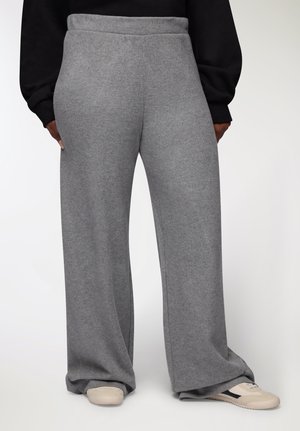 Pantaloni di tuta grigi a gamba larga con una morbida texture e vita elasticizzata, mostrati da dietro, abbinati a sneakers di colore chiaro.