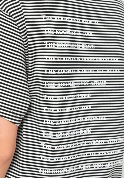 Mustriga must-valge T-särk, mille rinnal on tekstuuriga kiri "THE KOOPLES" erinevates pikkustes ja suundades.