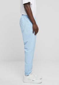 Light blue jogger pants with a textured finish, elastic waistband, side pockets, and tapered cuffs. Worn with white sneakers.