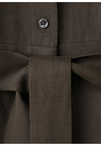 Dunkelbrauner, strukturierter Stoff mit einem gebundenen Gürtel und einem sichtbaren schwarzen Knopf, der im oberen Bereich angenäht ist.