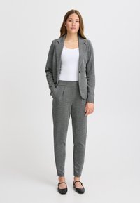 Grau karierter Anzugjacke mit Einzelknopfverschluss, kombiniert mit grauen, schmal geschnittenen Hosen. Ein einfaches weißes Oberteil und schwarze Ballerinas runden das Outfit ab.