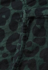 Zelená tkanina s černým leopardím potiskem. Má šev podél okraje a hladký, měkký povrch.