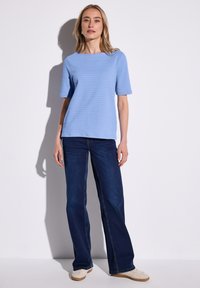 Ljusblå texturerad kortärmad topp i kombination med mörkblå utsvängda jeans och beige skor. Enkelt, strömlinjeformat design med en avslappnad passform.