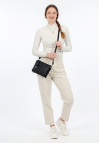 Borsa a tracolla in pelle nera con hardware argentato. Il modello indossa un dolcevita bianco a coste, pantaloni beige e sneakers bianche.