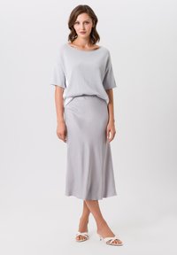 Haut à manches courtes gris clair avec une coupe décontractée, associé à une jupe longue et fluide dans une teinte assortie. Chaussures blanches à bout ouvert.