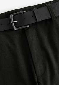 Czarne spodnie z tkaniny o teksturowanym wykończeniu, z czarnym skórzanym paskiem z metalową klamrą i regulowanymi otworami dla lepszego dopasowania.