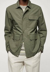 Giacca verde oliva in tessuto leggero, con colletto, bottoni a pressione frontali e due tasche applicate sul petto e sui lati.