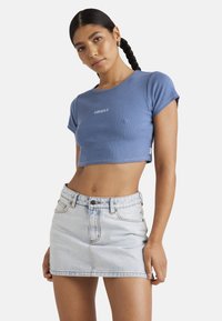 Crop top bleu à côtes avec des manches courtes et un logo blanc sur la poitrine, associé à une mini-jupe en denim clair avec des poches avant et des détails de couture.