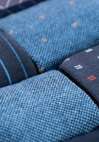 Mucchio di tessuti a maglia piegati di colore blu e nero, con motivi a pois e strisce, mostrati in dettaglio ravvicinato.