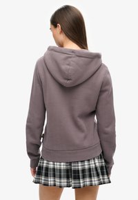 Grijze hoodie met een kangoeroezak, elastische manchetten en tailleband. Gecombineerd met een zwart-wit geruite plissérok.